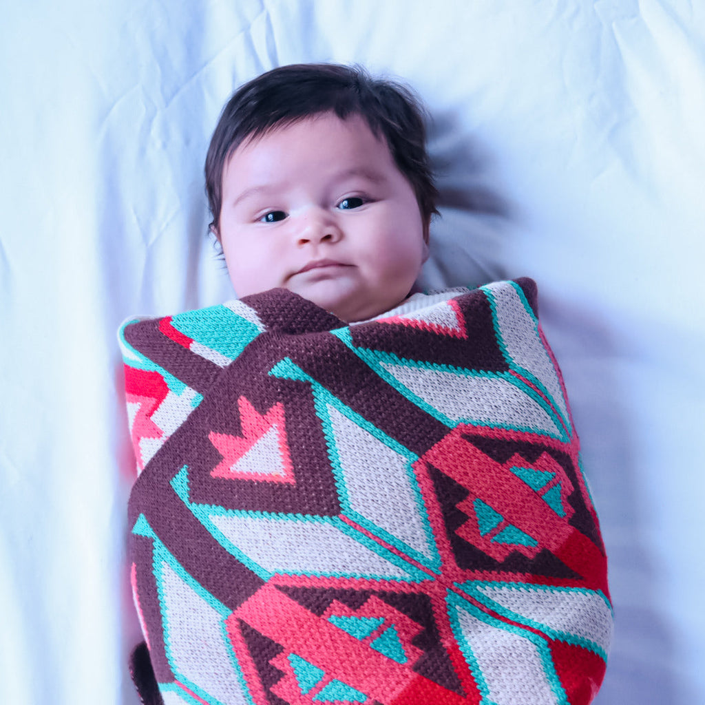 Baby wrapped in a colorful blanket with geometric patterns on a white background