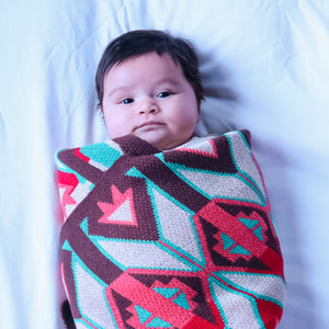 Baby wrapped in a colorful blanket with geometric patterns on a white background