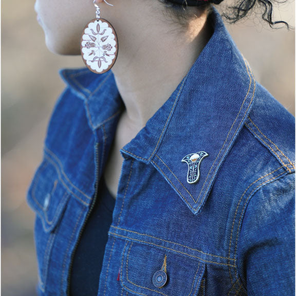 Person in jean jacket with Next Generation pin on left collar and Birch Bloom earrings