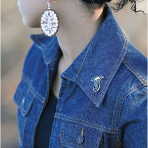 Person in jean jacket with Next Generation pin on left collar and Birch Bloom earrings